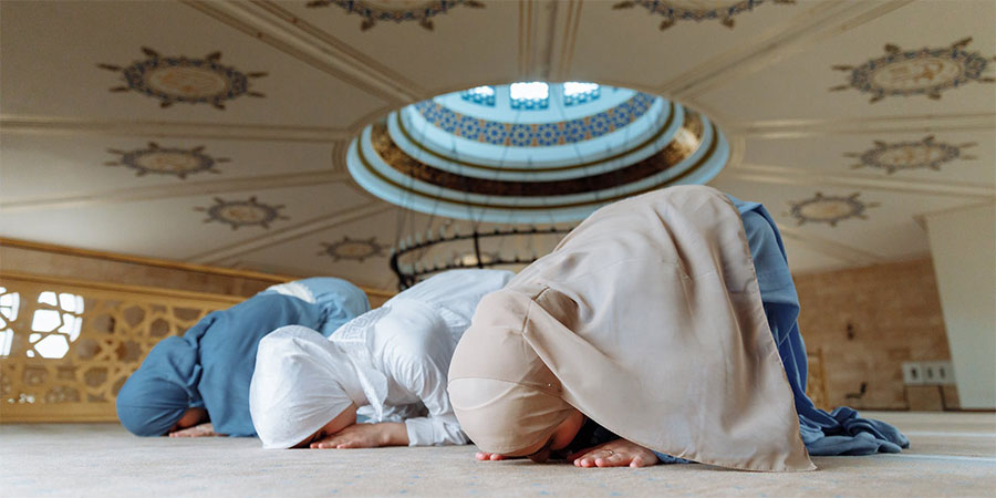 three woman wearing traditional clothing in a mosque bowing
